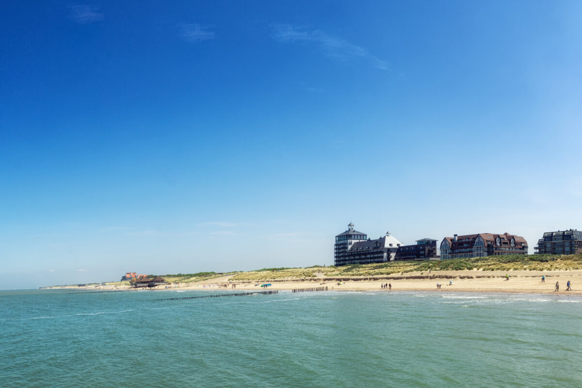 Panorama van het strand van Cadzand-Bad met helderblauw zeewater, zandduinen en moderne appartementengebouwen langs de kust.