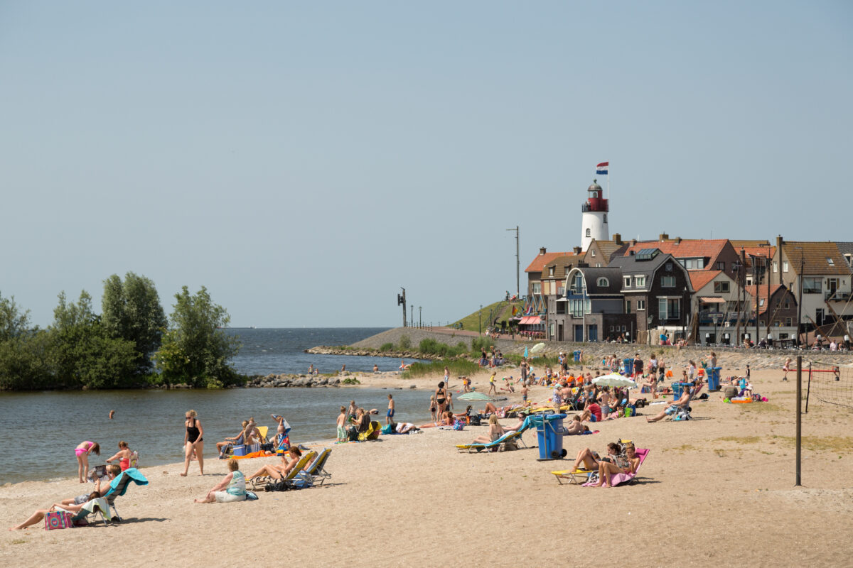 Kinderen en gezinnen genieten van het strand bij Urk, met op de achtergrond de karakteristieke vuurtoren en vissershuisjes.