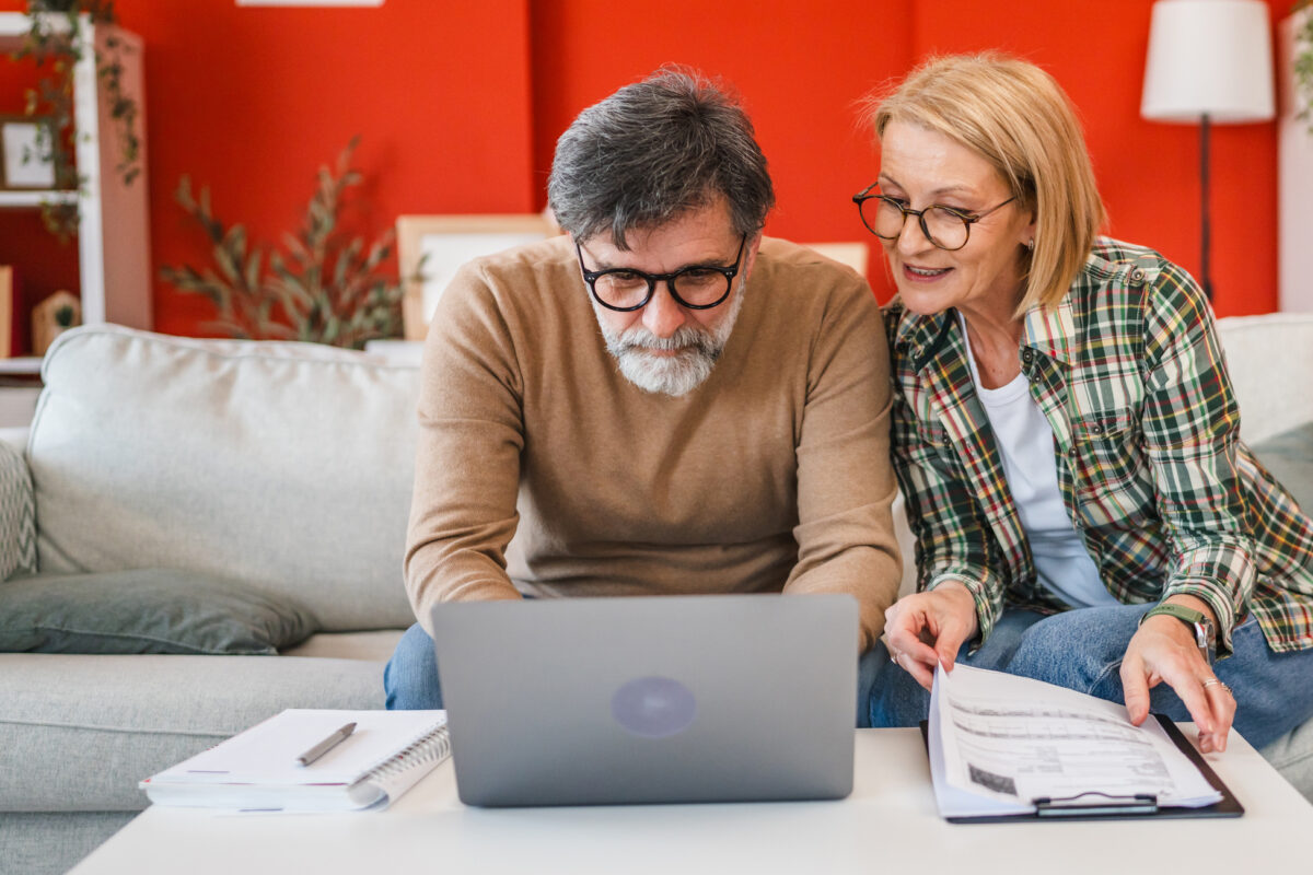 Twee verhuurders bekijken samen informatie over vakantieverhuur op een laptop en bespreken regels en administratie in hun woonkamer