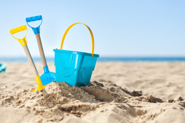 Blauwe emmer en schepjes in het zand op een zonnig strand aan zee – symbool voor kindvriendelijke stranddag in Nederland.