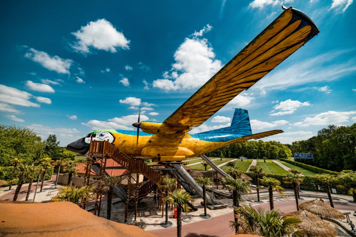 Groot kleurrijk vliegtuig in de vorm van een papegaai met glijbanen in pretpark Irrland onder een blauwe lucht.