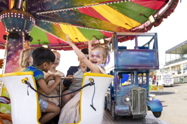Jonge kinderen met schmink lachen en zwaaien in een kleurrijke draaimolen