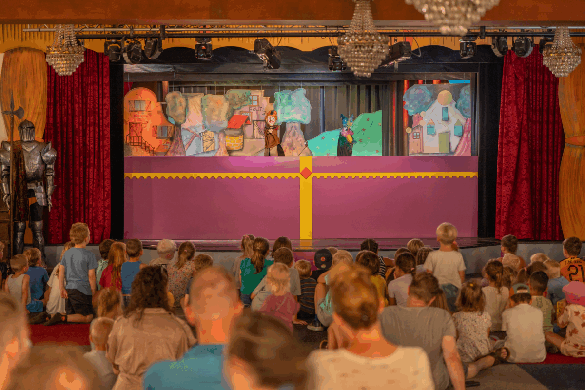 Kinderen kijken aandachtig naar een kleurrijke poppenkastvoorstelling van Jan Klaassen in het poppentheater, met vrolijk decor en handpoppen.