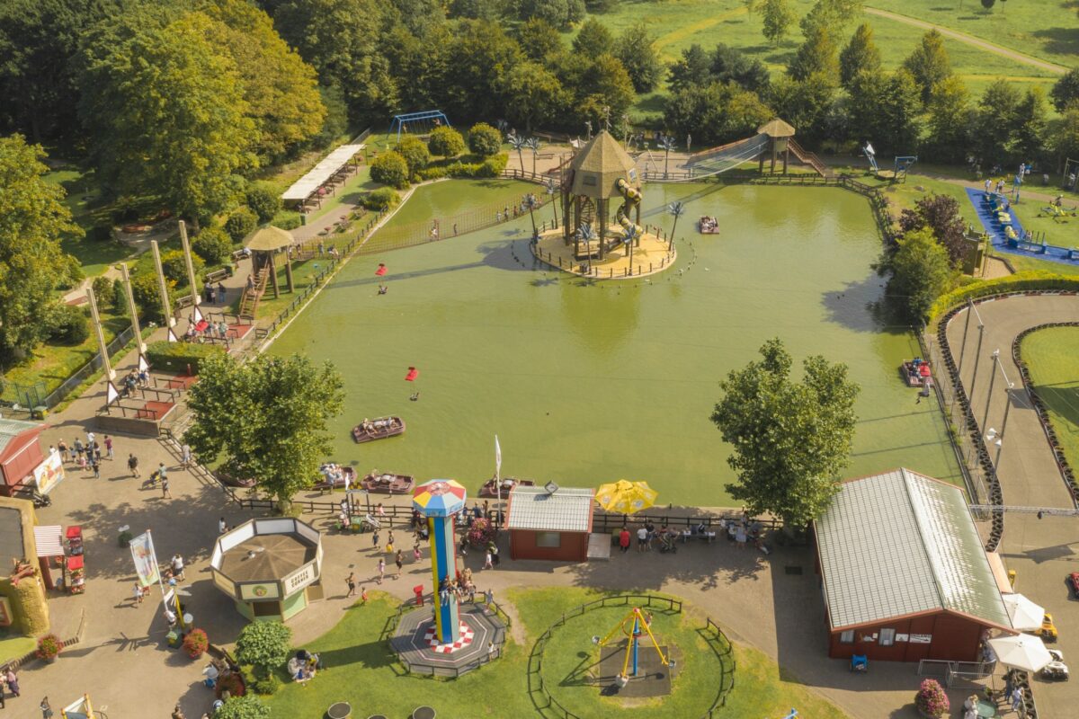 Luchtfoto van het Piraten-eiland in Linnaeushof, met kinderen die spelen in bootjes op het water en op de grote houten klim- en speeltoestellen.