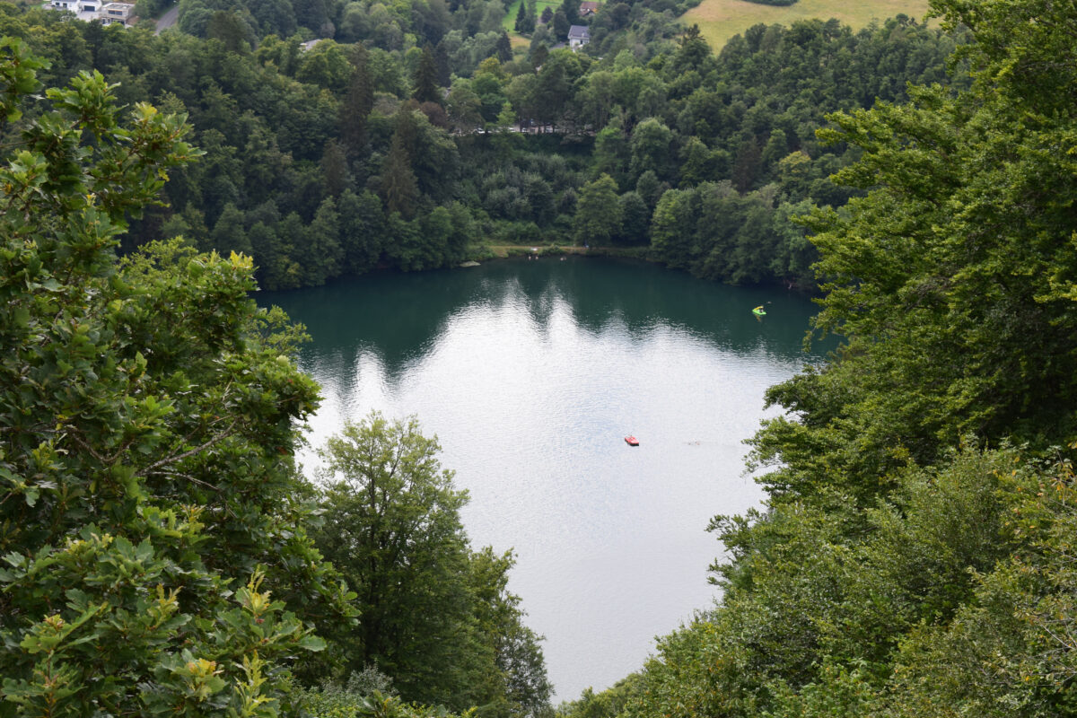 Uitzicht op een van de maaren in de Vulkaaneifel in Duitsland, een rond kratermeer omringd door dicht bos en groene heuvels.