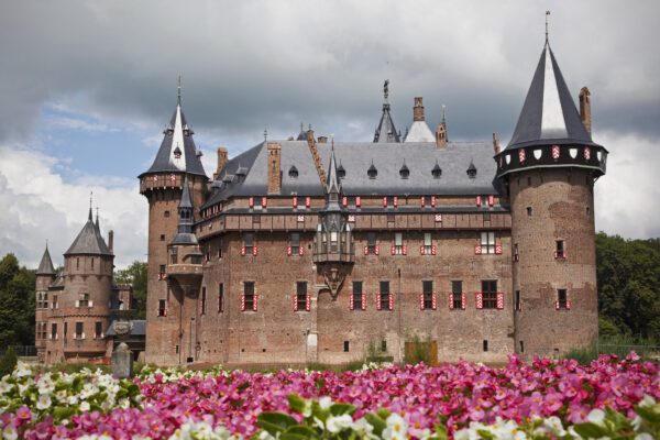 Kasteel De Haar in Utrecht, een imposant roodstenen kasteel met torens en bloemenperken op de voorgrond.