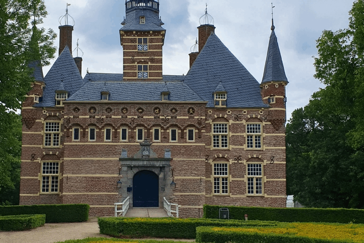 Voorgevel van Kasteel Wijchen met zijn kenmerkende torens, rood-witte baksteen en omliggende tuinen.